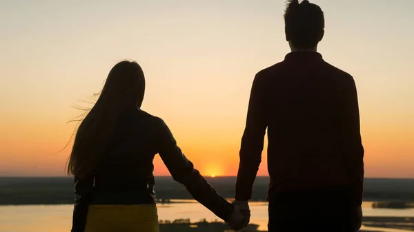 Любящие молодые пары держатся за руки, глядя друг на друга на удивительный закат на открытом воздухе - закрыть — стоковое фото