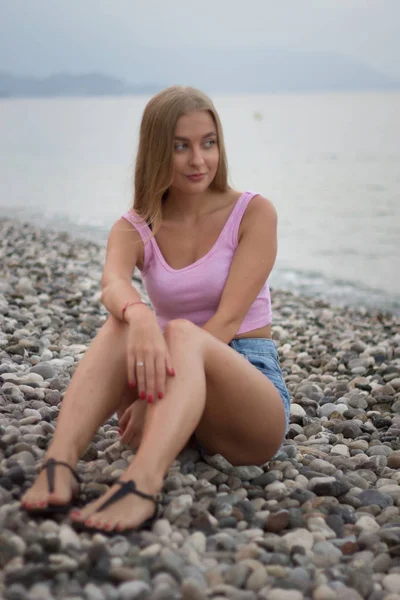 Vista posteriore della giovane donna bionda seduta sulla spiaggia di pietra — Foto Stock