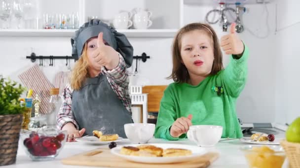 Two preschool girls bakers eats cooked cheesecakes and shows big finger up — Stock Video