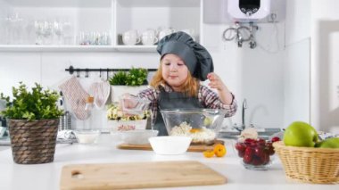 Küçük kız baker mutfak üzerinde yumurta bisküvi yemek pişirmek için pasta hamur koyar
