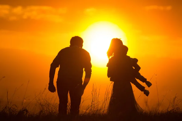 Parents avec un bébé dans la prairie de coucher de soleil d'été - silhouette — Photo