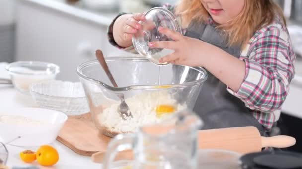 Little girl baker on kitchen puts eggs to the pastry dough for cooking biscuits — Stock Video