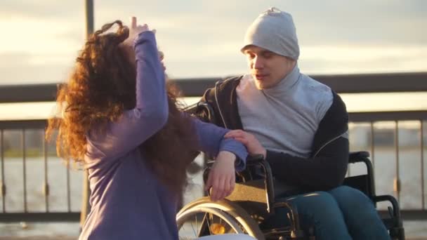 Couple heureux - homme handicapé en fauteuil roulant parlant avec une jeune femme attrayante profitant du coucher du soleil — Video