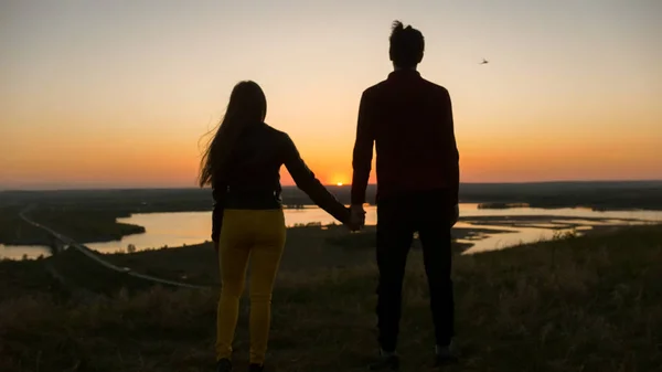 Liefdevolle jonge paar hand in hand elkaar kijken naar geweldige zonsondergang buitenshuis - close up — Stockfoto