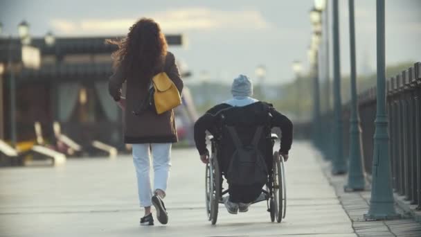 Joven mujer feliz con hombre discapacitado en una silla de ruedas caminando juntos en el muelle — Vídeos de Stock