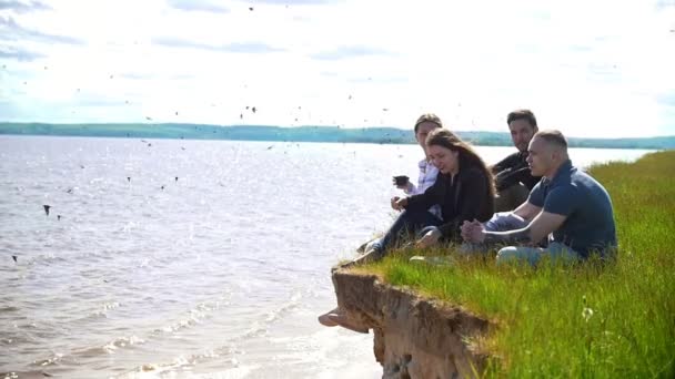 Jovens amigos sentados na colina sobre o rio desfrutando de fim de semana na natureza — Vídeo de Stock