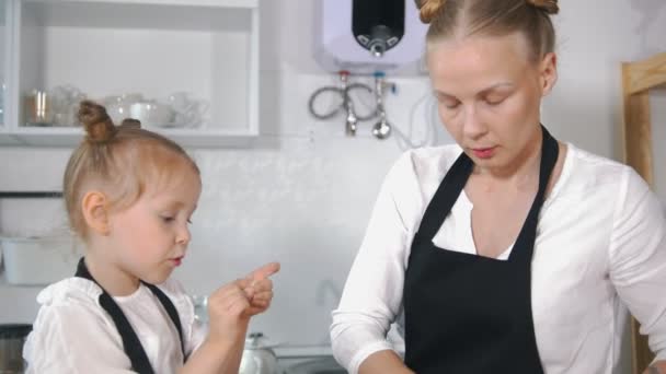 Liten flicka talar med sin mor som matlagning keso pannkakor i köket — Stockvideo