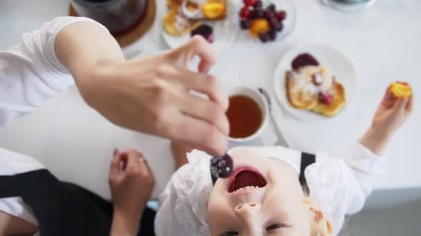 Bovenaanzicht van de moeder en haar kleine meisje thee drinkt en eet cherry — Stockvideo