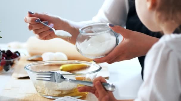 Vrouw met haar kind zet suiker in het deeg voor het voorbereiden van pannenkoeken — Stockvideo