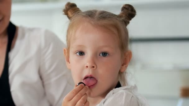 Cheerful little girl licks a berry and looking at the camera — Stock Video