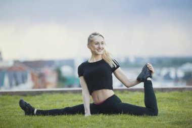 Mutlu genç kadınla çimenlerin üzerinde sicim bükülmüş bacak ile arka plan cityscape üzerinde gerçekleştirir.