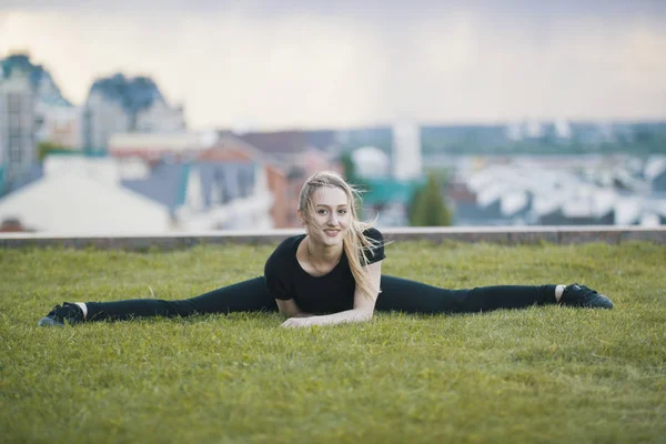 Sonriente chica joven en la hierba verde realiza cordel, en el paisaje urbano de fondo —  Fotos de Stock