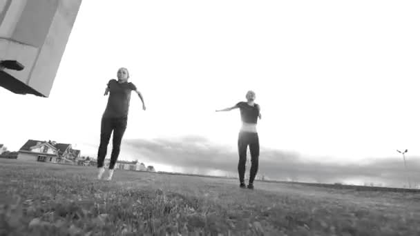 Dos mujeres jóvenes acrobat entrenamiento al aire libre en el paisaje urbano de fondo — Vídeos de Stock