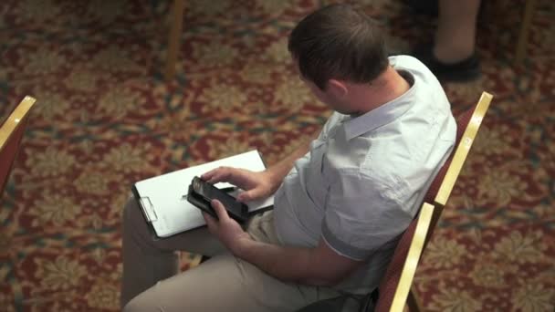 Vista superior del hombre sentado con una hoja de papel y la escritura por teléfono en la conferencia de negocios — Vídeos de Stock