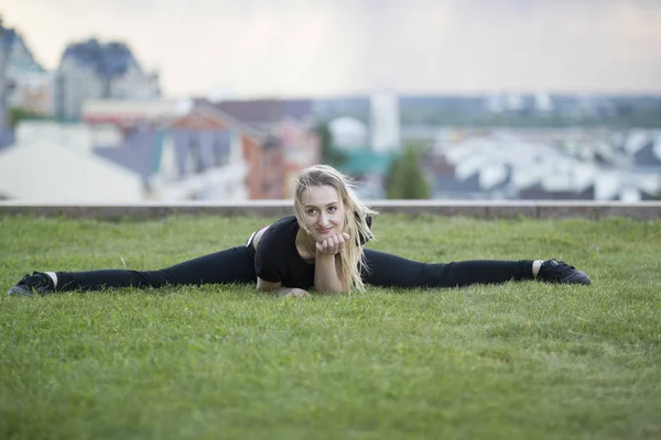 Sonriente chica joven en la hierba verde realiza cordel, en el paisaje urbano de fondo — Foto de Stock