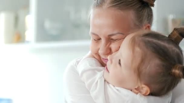 Веселая маленькая девочка обнимает свою мать на кухне — стоковое видео