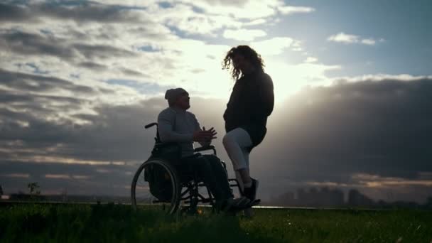 Zorg voor mensen met een handicap - man in een rolstoel met vrouw praten op de bewolkt zonsondergang — Stockvideo