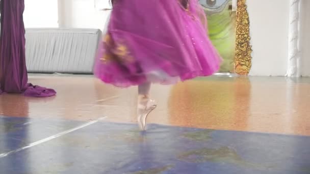 Ноги балерини на взутті в фіолетовій пишній спідниці, що крутиться в просторій білій студії — стокове відео