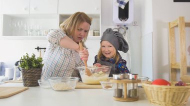 Neşeli küçük kız annesiyle bisküvi yemek pişirmek için cam kase hamur karıştırma