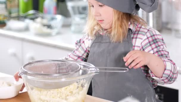 Маленька мила дівчинка шеф-кухар готується просіяти борошно через сито — стокове відео