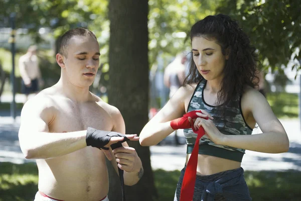 Hombre boxeador envolver sus manos joven mujer le ayuda, entrenamiento en el parque —  Fotos de Stock