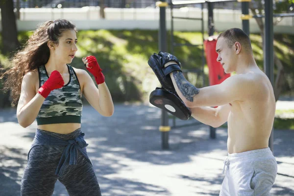 Genç adam güzel bir kadın boks açık havada güneşli gün, yatay darbeler öğretir