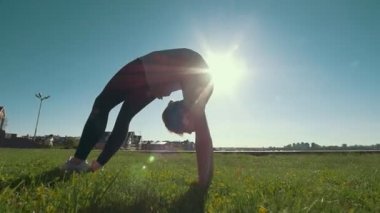 Genç kadın jimnastikçi jimnastik Köprüsü çimlere güneşli gün yapar