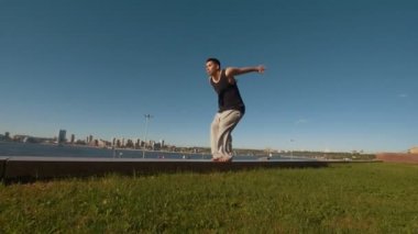 Genç adam akrobatik flip nehir ve cityscape bakan sarp bir kayalığın kenarına gerçekleştirir.