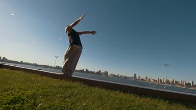 Genç adam profesyonel acrobat bir flip nehir ve cityscape günbatımında bakan sarp bir kayalığın üzerinde gerçekleştirir