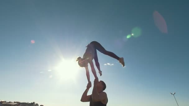 Jovem casal acrobático realizando flip, jovem joga uma mulher no ar equilibrando em seus braços ao pôr do sol ao ar livre — Vídeo de Stock