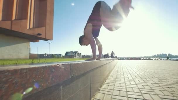 Homem acrobático jovem executa um suporte no passeio ao ar livre ao pôr do sol — Vídeo de Stock