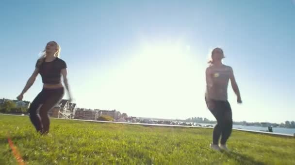 Dos mujeres jóvenes realizando cordel en saltos al aire libre bajo el sol — Vídeos de Stock