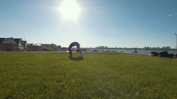 Jonge vrouwelijke turnster voert gymnastische brug op het gras in zonnige dag — Stockvideo