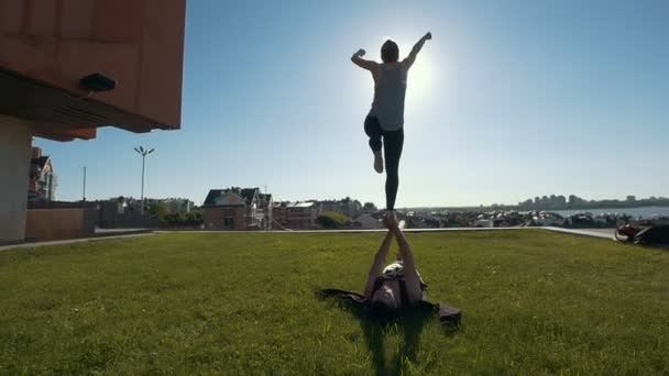 Joven pareja deportiva practicando acrobacias realizando pose de pájaro de tablón delantero, joven hombre sosteniendo mujer voladora balanceándose en sus brazos al aire libre al atardecer — Vídeos de Stock