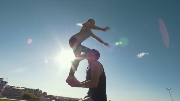 Молодая пара практикует акробатику, выполняя трюки на открытом воздухе на закате — стоковое видео