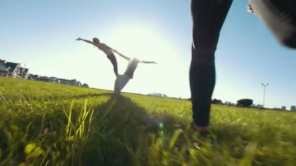 Benen van jonge vrouw wandelingen vooruit naar tiener team presteert cheerleading trucs op het gras onder de zon — Stockvideo