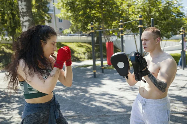 Joven hombre enseña hermosa mujer boxeo golpes al aire libre en día soleado —  Fotos de Stock