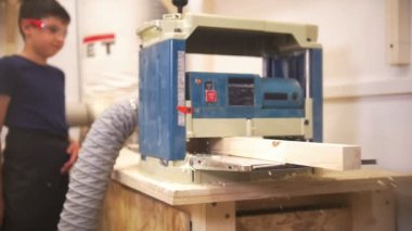 Usta bir ahşap kiriş yakın duran ve izlerken makine, Genç çocuk taşlama marangozluk aracılığıyla geçer