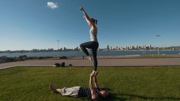 Ung sportig par öva akrobatik utför främre planka fågel pose, ung man håller flygande kvinna balansera på armarna utomhus i solnedgången — Stockvideo