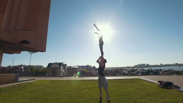 Pareja joven practicando acrobacias realizando pose de pájaro de tablón delantero, hombre joven levanta a mujer joven voladora balanceándose en sus brazos al atardecer — Vídeos de Stock