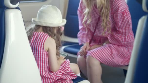 Vista trasera de la niña utilizar un teléfono inteligente y sentado en el sillón delante de su madre en el tren — Vídeos de Stock