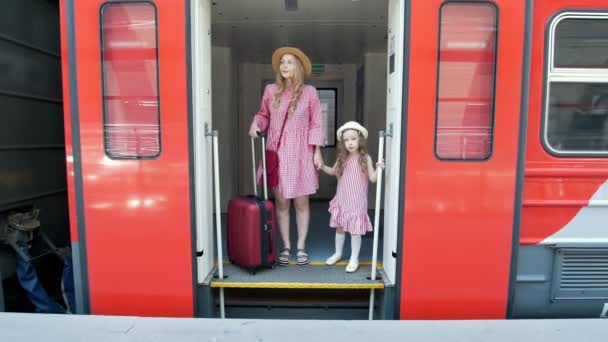 Mujer joven con maleta y su hija pequeña sale del vagón del tren — Vídeo de stock