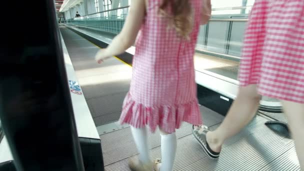 Vista trasera de mamá y su hija bajando por la escalera mecánica en el aeropuerto — Vídeo de stock