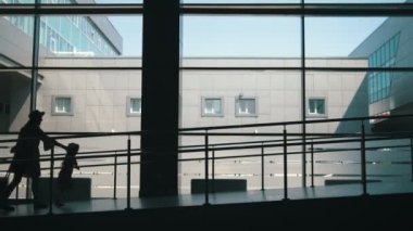 Anne ve küçük kızı arka plan büyük pencere havaalanında kapıda aşağı gidiş siluetleri