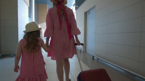 Rear view of young mother and cute daughter holding hands walking at corridor at the airport — Stock Video