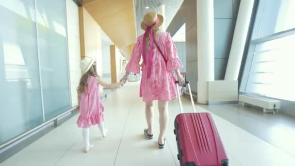 Rear view of mother and little daughter holding hands walking to the waiting room in airport — Stock Video