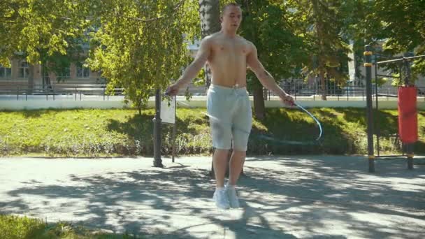 Homem muscular atlético pulando com uma corda, treino ao ar livre no dia ensolarado - câmera lenta — Vídeo de Stock