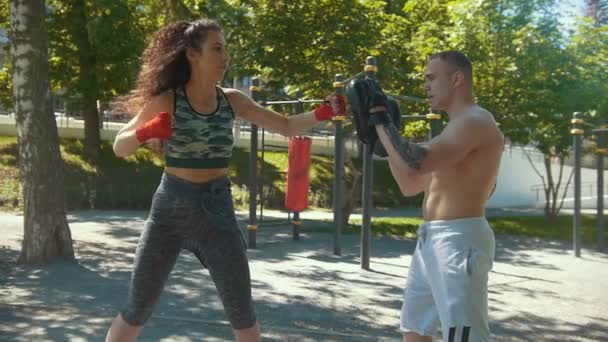 Young man teaches beautiful woman boxing blows outdoors at sunny day, slow-motion — Stock Video