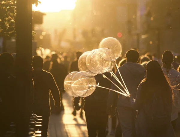 Mujer joven con globos caminando en multitud en la calle peatonal al atardecer de verano — Foto de Stock