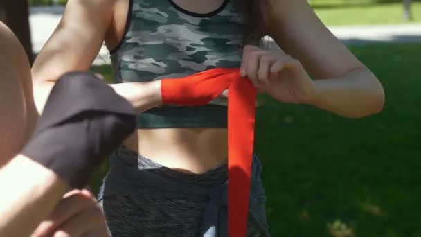 Руки молодого мужчины и женщины, обертывающие руки бинтами для тренировки в летний день — стоковое видео